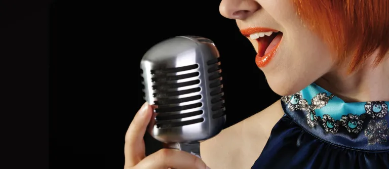 Mulher cantando em palco, representando o Curso de Canto Iara Negrete - Além da Voz